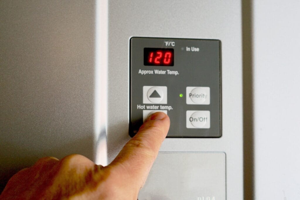 Finger adjusting hot water heater control unit, displaying temperature setting of 120°F, relevant to plumbing maintenance and water heater management tips.