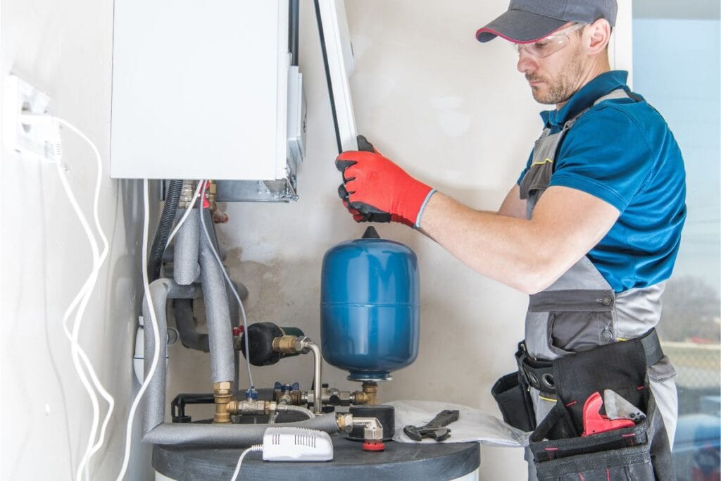 7 Signs It’s Time to Replace Your Water Heater 3 A worker in protective gear carefully adjusts equipment on a heating system, mindful of when to replace the water heater to ensure efficiency and safety.