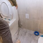 Toilet installation in a bathroom renovation, showcasing plumbing connections and flooring.