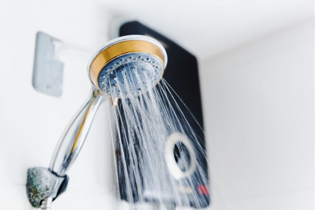 7 Signs It’s Time to Replace Your Water Heater 4 A showerhead sprays water in a bathroom, with a water heater in the background, subtly reminding you it's crucial to know when to replace your water heater for optimal efficiency.