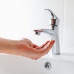Hand reaching for water from a modern faucet, illustrating plumbing issues related to low water pressure and the importance of proper maintenance.