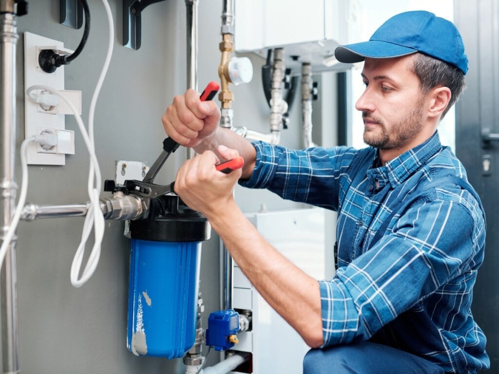 Plumber using tools to repair a water filtration system, showcasing advanced leak detection techniques relevant to JW Plumbing Pros' services.