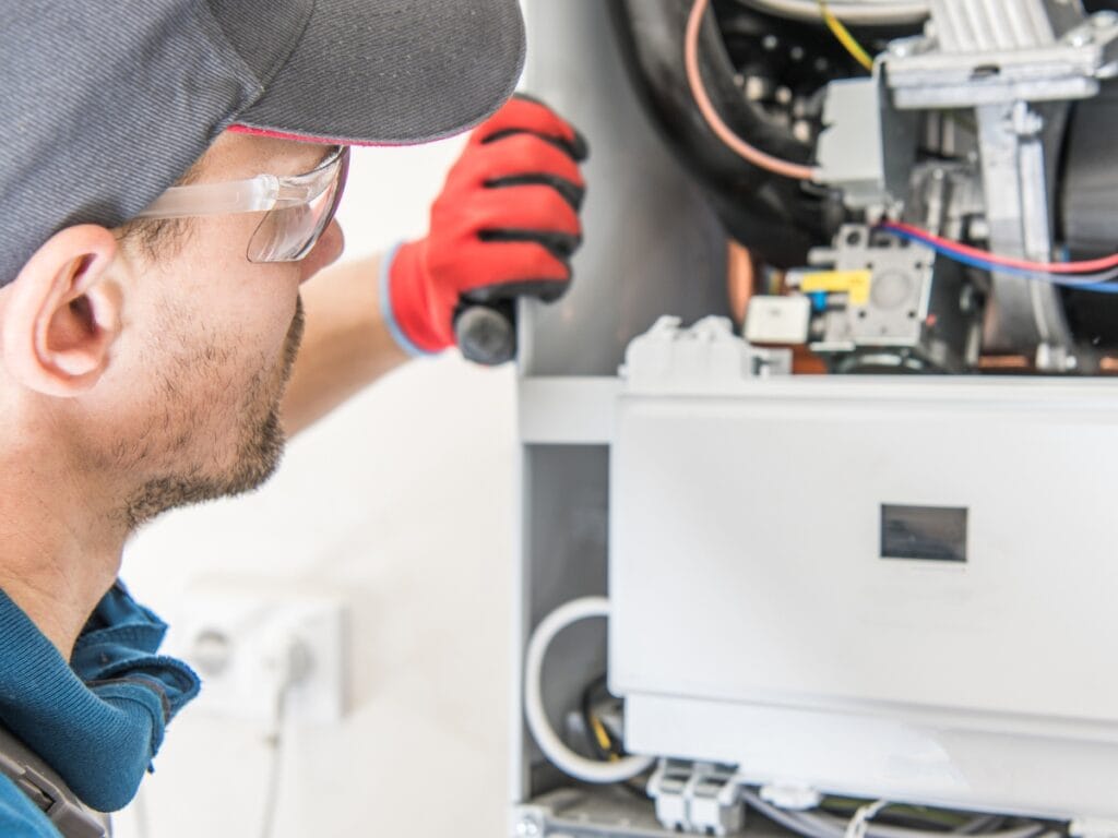 A technician wearing safety glasses and gloves inspects or repairs the inside of a gas boiler, helping homeowners make important water heater replacement decisions.