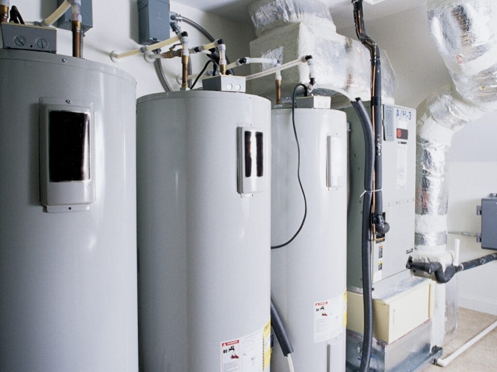 Three water heaters and an HVAC unit are installed in a utility room with visible pipes, ducts, and insulation—ideal for assessing Water Heater Repair or making a Water Heater Decision.