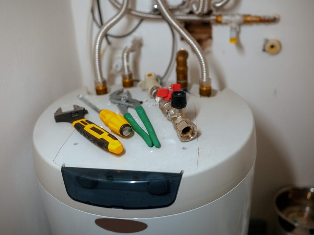 Benefits of Tankless Water Heaters for Energy-Efficient Homes 9 A tankless water heater with various plumbing tools, including a wrench, pliers, screwdriver, and utility knife, rests on top. Several pipes and valves are visible above the unit—ideal for energy-efficient homes seeking modern benefits.